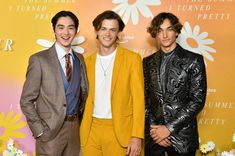 three young men standing next to each other in front of a flowery wallpaper