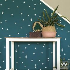 a white table topped with a potted plant next to a wall covered in triangles