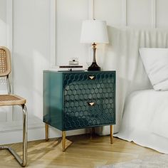 a bedroom with a bed, nightstand and chair next to each other in front of a white wall