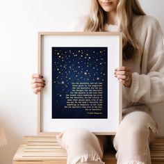 a woman sitting on a wooden bench holding up a framed print with the words, and stars