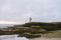 two people are standing on the rocks by the water