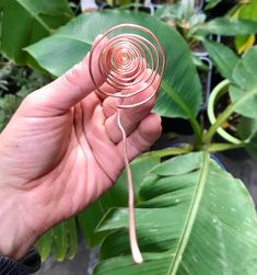 a hand holding a metal object in front of some plants