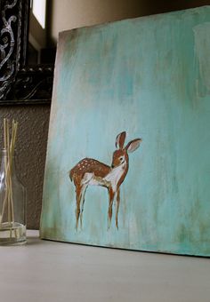 a painting of a deer on a blue background next to a glass vase with reeds