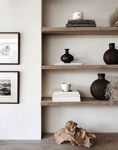 some vases are sitting on shelves in a room with white walls and wood flooring