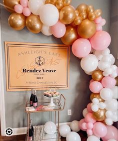 an arch made out of balloons and wine bottles is displayed in front of a sign