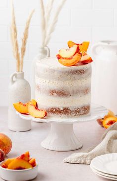 a white cake with peaches on top sitting on a table next to other plates and bowls