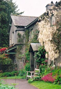 the house is surrounded by beautiful flowers and greenery, with a bench in front