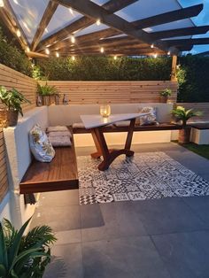 an outdoor dining area with wooden benches and lights on the roof, surrounded by greenery