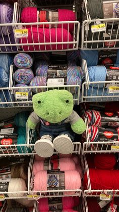 a teddy bear sitting on top of a shelf in a yarn store next to some crochet