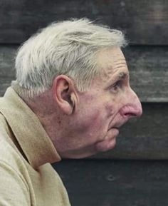 an older man with white hair is looking off into the distance while wearing a tan sweater