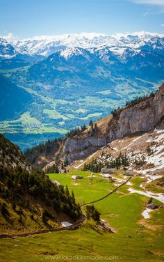 a valley with snow capped mountains in the distance and green grass on the ground below