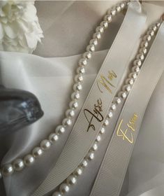 two pearls are attached to a white ribbon with gold writing on it and the bride's name