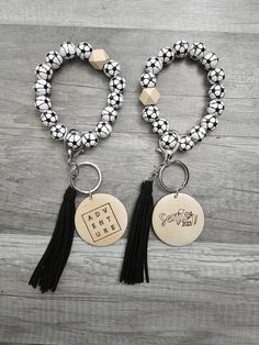 two black and white bracelets with tassels, one has a charm that says we are here