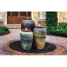 two large vases sitting on top of each other in front of a house with landscaping around them