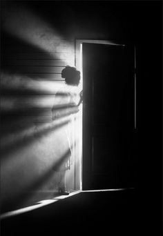 a person standing in front of a door with the light coming through it and their shadow on the wall