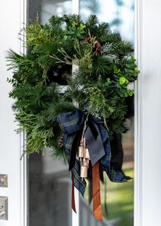 a wreath hanging on the front door of a house with ribbon tied around it's neck