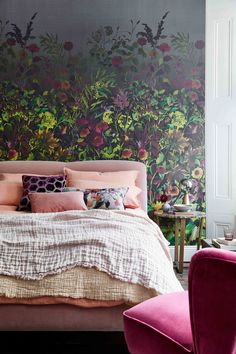 a bedroom with floral wallpaper and bedding in the foreground is a pink chair