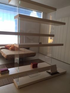 a bed sitting in the middle of a room next to a window with lots of books on it