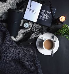 a cup of coffee next to an open book and some other items on a table