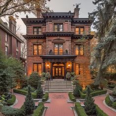 a large brick house with lots of trees and bushes in front of it at dusk