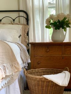 a bedroom with a bed, basket and flowers on the nightstand next to the window