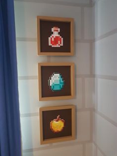 three pixel art pieces hanging on the wall above a toilet in a room with blue curtains