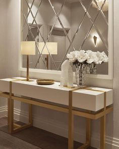 a white table topped with a vase filled with flowers next to a mirror and lamp