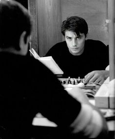 a man sitting at a table with a chess board in front of him and another man standing next to him