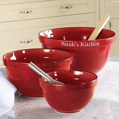 three red bowls with spoons in them sitting on a kitchen counter next to towels