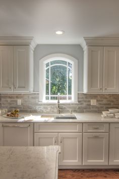 a kitchen with white cabinets and marble counter tops, an arched window over the sink