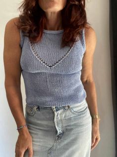 an older woman with red hair wearing a blue tank top and denim skirt standing in front of a window