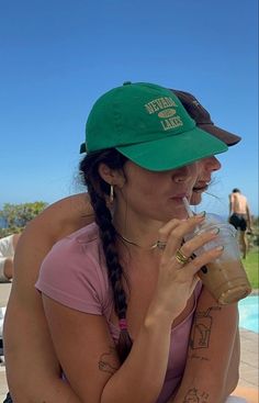 a woman sitting at a table with a drink in her hand while wearing a green hat