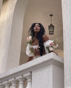 a woman with long hair standing on a balcony next to a lamp post and flowers