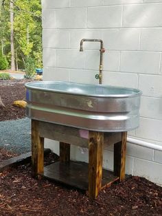 a metal sink sitting on top of a wooden stand next to a white brick wall