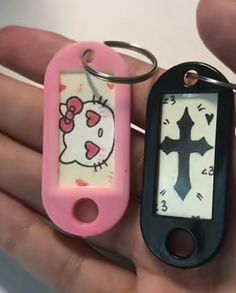 two hello kitty keychains in the palm of someone's hand, one with a cross on it