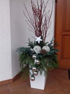 a white planter filled with ornaments and greenery next to a door on a tile floor