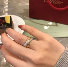 a woman's hand with a ring on top of her finger next to a piece of cake