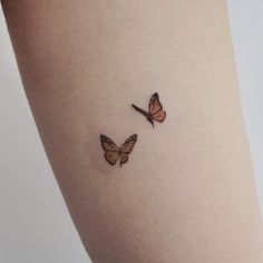 two small butterflies on the side of a woman's thigh, one is orange and the other is brown