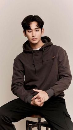 a young man sitting on top of a stool wearing a brown sweatshirt and black pants