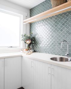 a kitchen with white cabinets and green tiles on the backsplash, along with a stainless steel sink