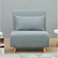 a gray chair sitting on top of a wooden floor next to a book shelf and table