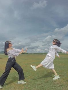 two young women are playing with a frisbee in the grass on a cloudy day