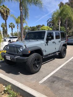 a gray jeep parked in a parking lot next to palm trees and other cars on the street