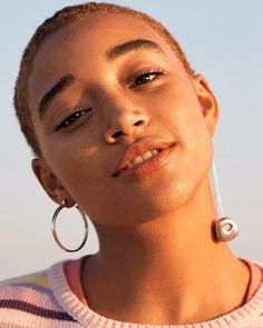 a close up of a person wearing large hoop earrings and a striped shirt with the sun shining on her face