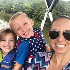 a woman and two children are on a boat in the water with trees in the background