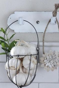 some garlic is in a wire basket next to a wall hook on a white brick wall