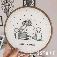 a person holding up a cross - stitch hoop with a drawing of a family on it