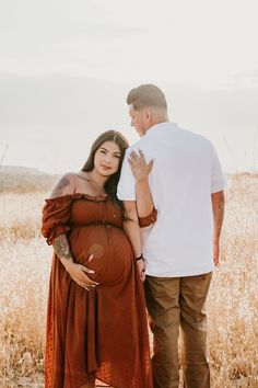 a pregnant woman standing next to a man in a field