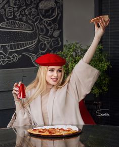 a woman sitting at a table holding up a slice of pizza