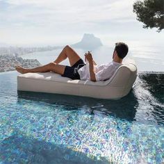 a man sitting on an inflatable lounge chair next to the pool looking out at the ocean